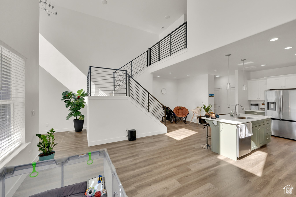 Kitchen with appliances with stainless steel finishes, a sink, light wood finished floors, a kitchen bar, and a high ceiling