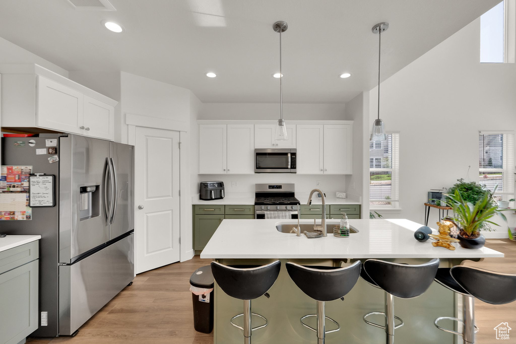 Kitchen featuring stainless steel appliances, a sink, light countertops, a kitchen breakfast bar, and light wood finished floors