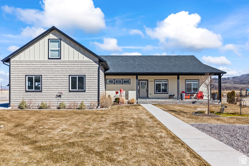 View of front of home with a porch, a front lawn, board and batten siding, and roof with shingles