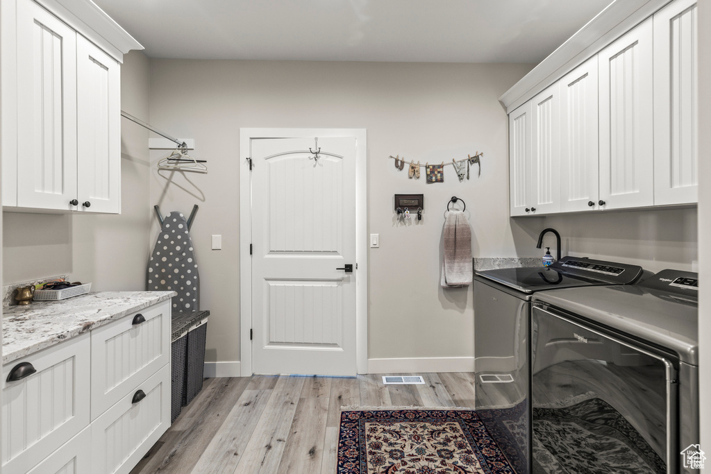 Washroom with cabinet space, washer and dryer, light wood finished floors, and baseboards