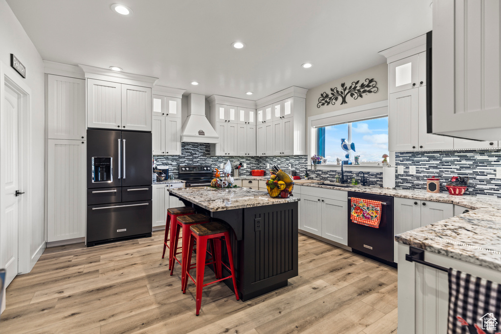 Kitchen featuring black appliances, custom exhaust hood, a sink, backsplash, and light wood-style floors