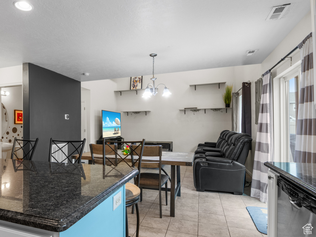 Kitchen featuring a breakfast bar area, light tile patterned flooring, open floor plan, dark stone counters, and hanging light fixtures