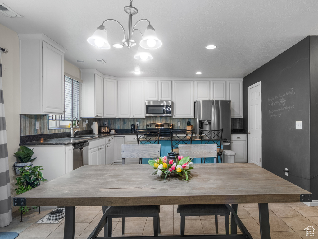 Kitchen featuring appliances with stainless steel finishes, dark countertops, a sink, a chandelier, and white cabinetry