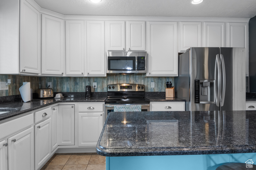 Kitchen with appliances with stainless steel finishes, white cabinetry, light tile patterned flooring, and dark stone counters