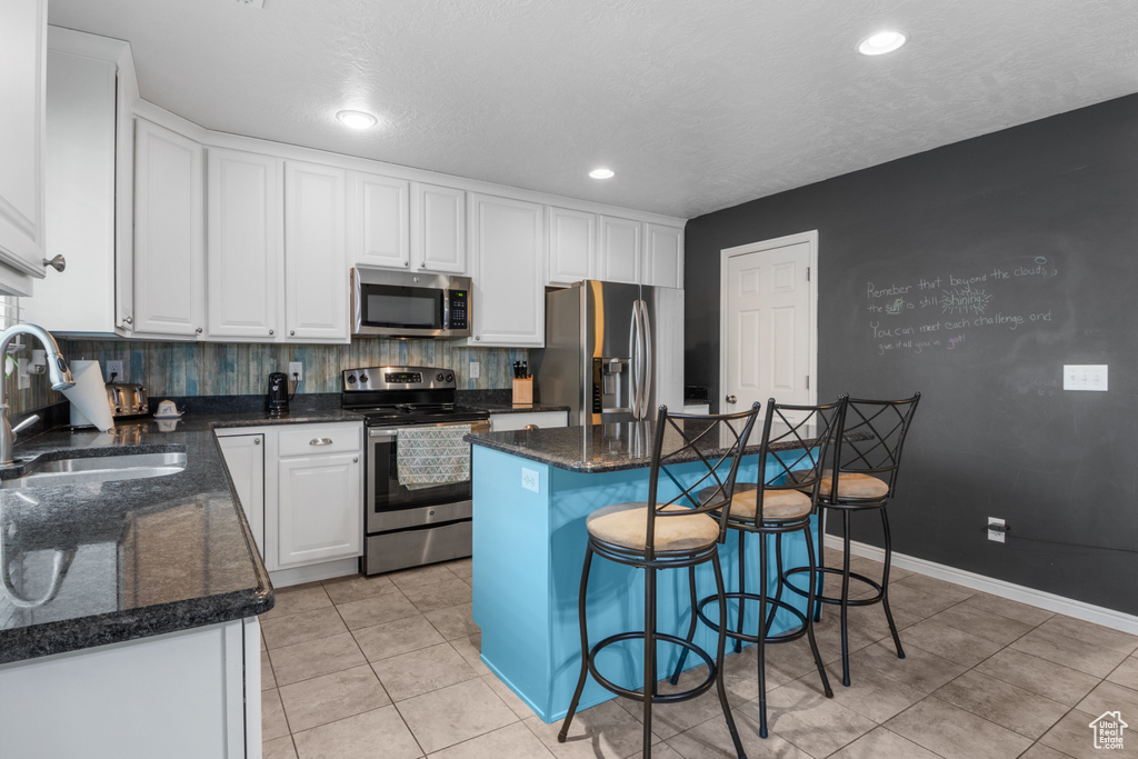 Kitchen featuring stainless steel appliances, a sink, white cabinetry, a center island, and light tile patterned floors