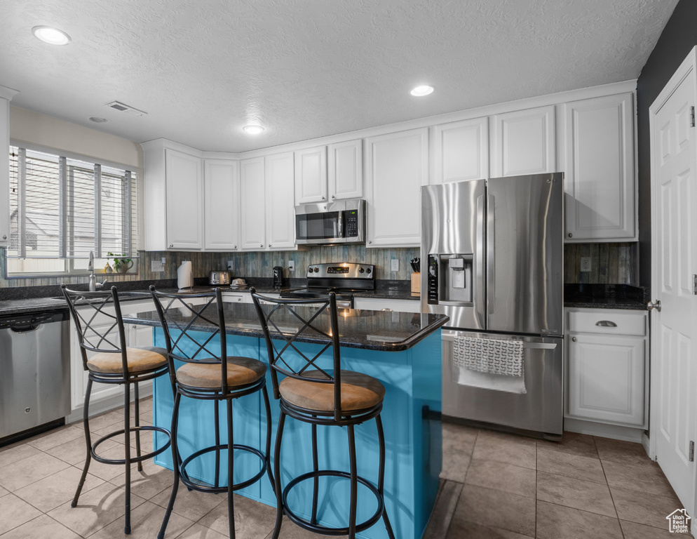 Kitchen featuring stainless steel appliances, a textured ceiling, tasteful backsplash, white cabinetry, and recessed lighting