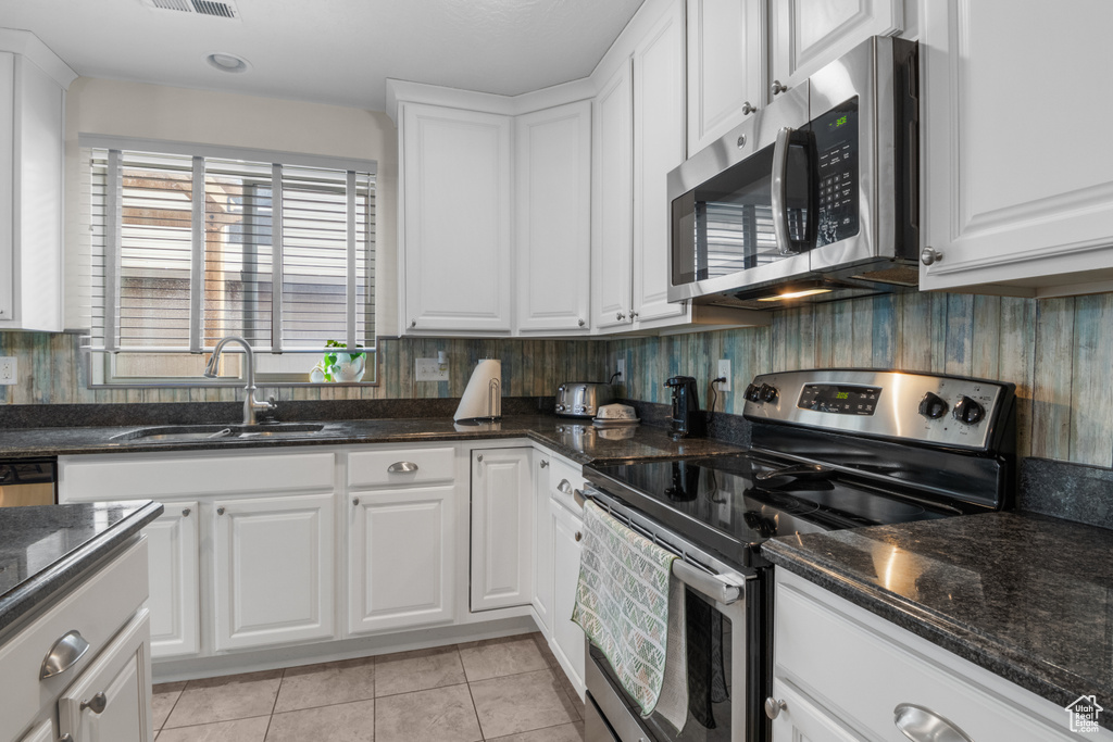 Kitchen featuring stainless steel appliances, a sink, white cabinetry, light tile patterned floors, and dark stone counters