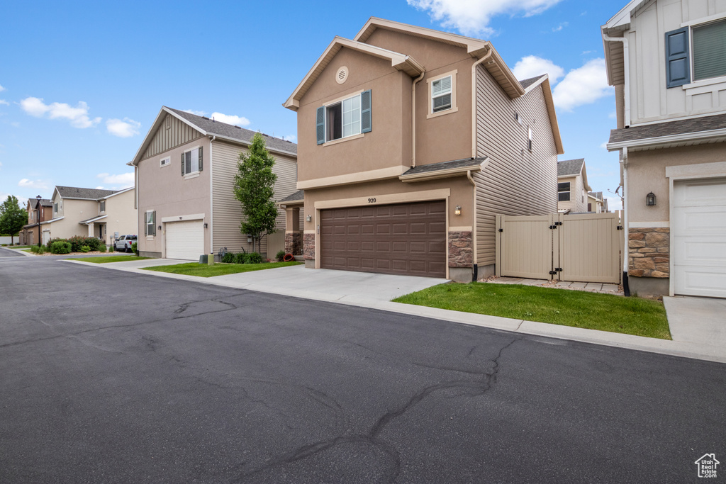 View of front of home featuring a garage, a residential view, concrete driveway, a gate, and stone siding