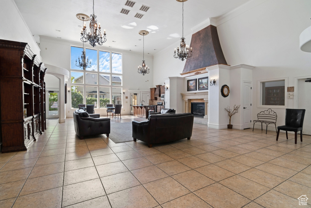 Living room featuring a high ceiling, a chandelier, light tile patterned flooring, a glass covered fireplace, and ornamental molding