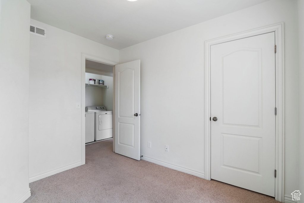 Unfurnished bedroom with light carpet, washing machine and dryer, and baseboards