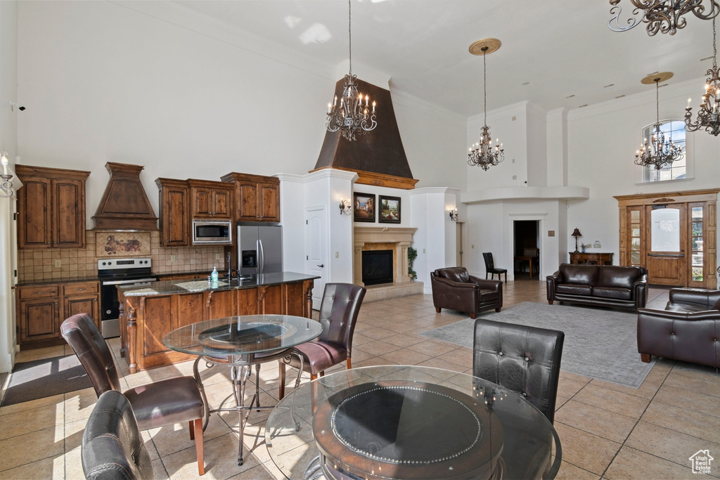 Dining area with a chandelier, a towering ceiling, a large fireplace, light tile patterned floors, and ornamental molding