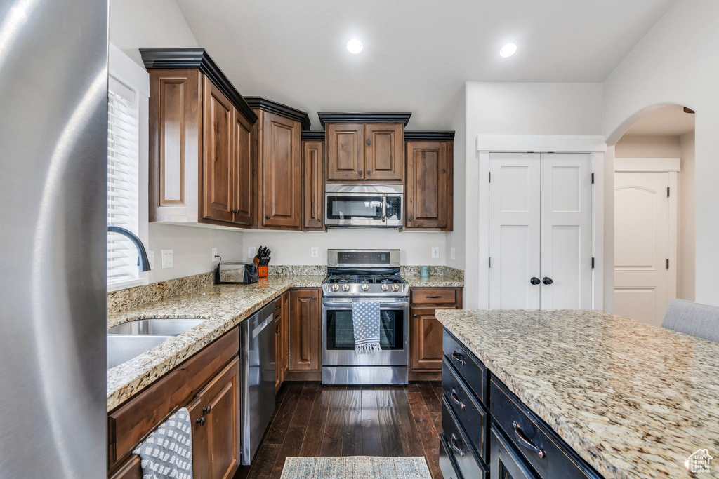 Kitchen featuring appliances with stainless steel finishes, a sink, arched walkways, dark wood-type flooring, and light stone countertops