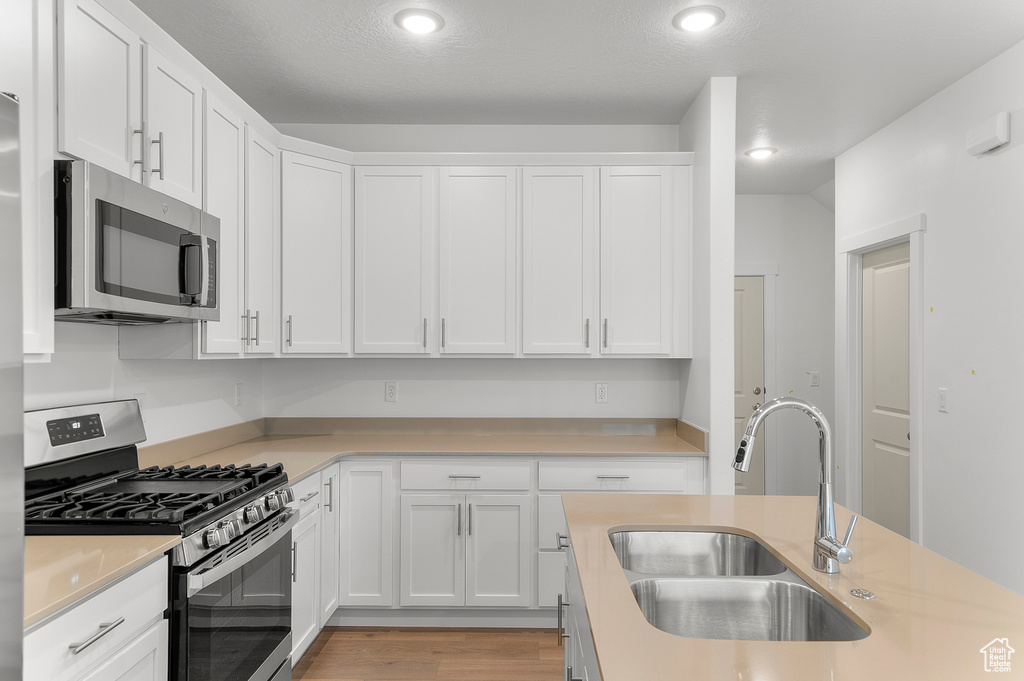 Kitchen with stainless steel appliances, a sink, light countertops, white cabinetry, and recessed lighting