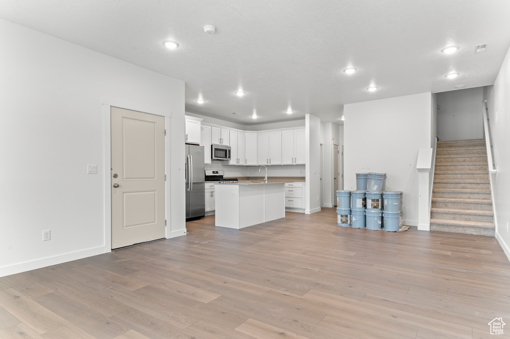 Unfurnished living room featuring a sink, stairs, light wood finished floors, baseboards, and recessed lighting