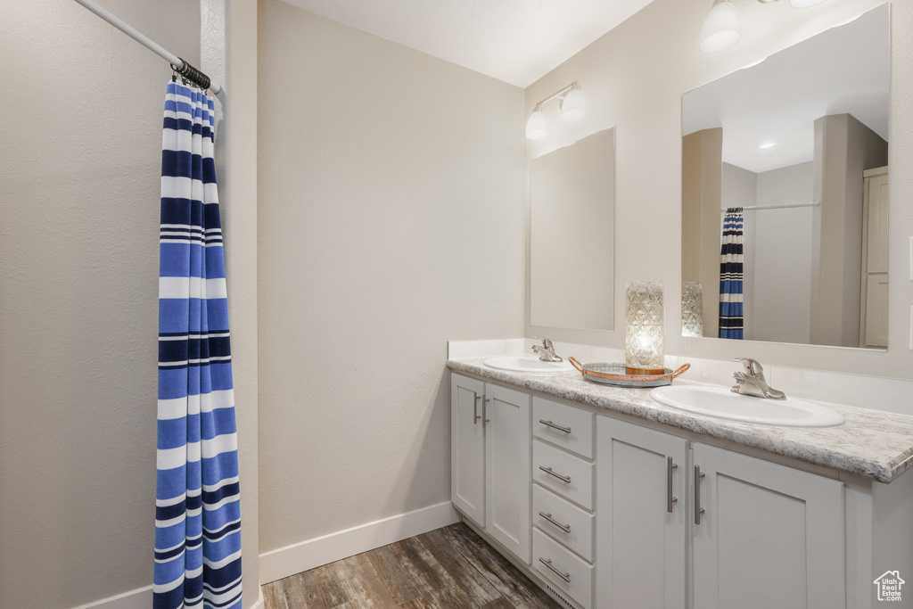 Bathroom with baseboards, wood finished floors, double vanity, and a shower with shower curtain