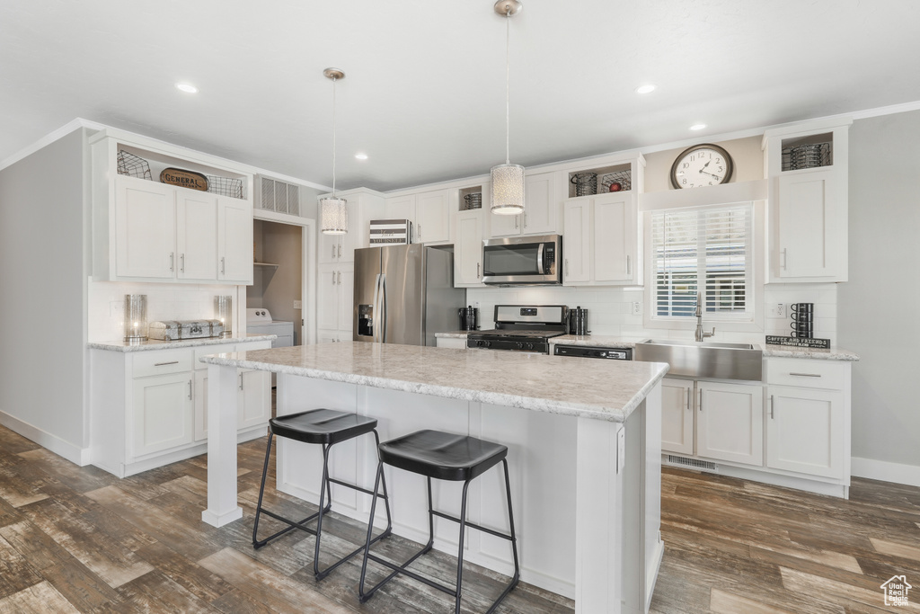 Kitchen featuring appliances with stainless steel finishes, a sink, a breakfast bar, white cabinets, and recessed lighting
