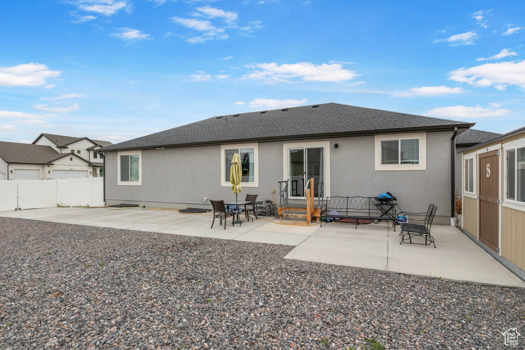 Rear view of property featuring stucco siding, a patio area, fence, and a shingled roof