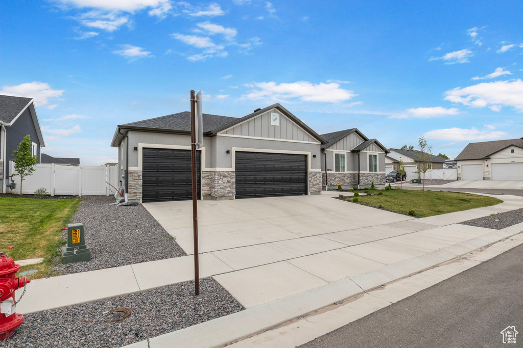 View of front of home featuring an attached garage, board and batten siding, stone siding, driveway, and a gate
