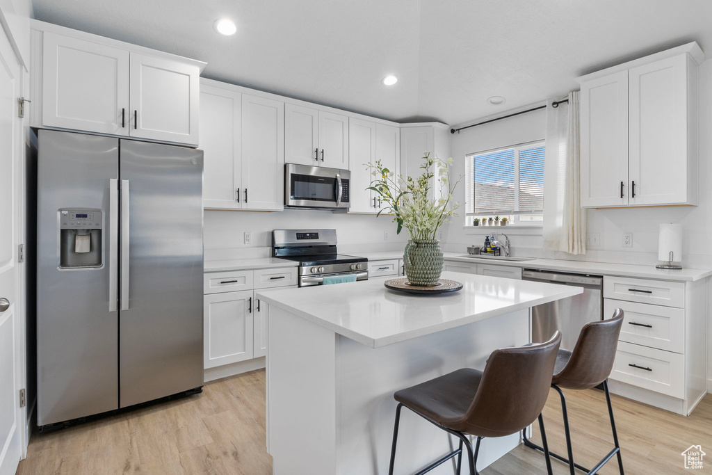Kitchen with stainless steel appliances, a sink, a kitchen breakfast bar, white cabinets, and light wood-style floors