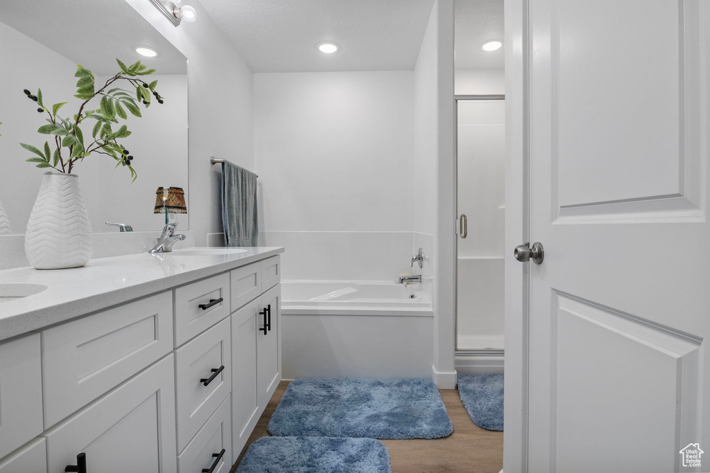 Full bathroom with a stall shower, wood finished floors, a garden tub, double vanity, and recessed lighting