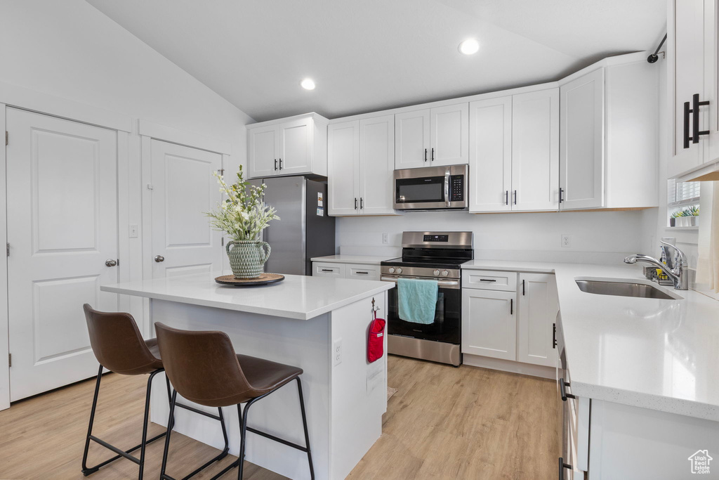 Kitchen featuring stainless steel appliances, a sink, lofted ceiling, a kitchen bar, and white cabinets