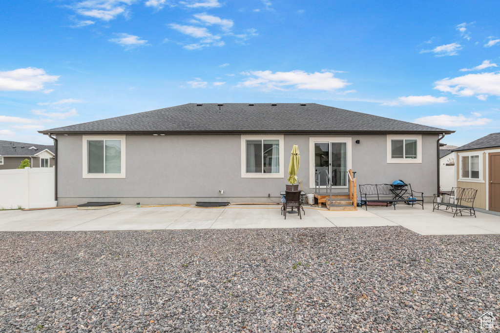 Rear view of house featuring stucco siding, fence, a patio, a shingled roof, and entry steps