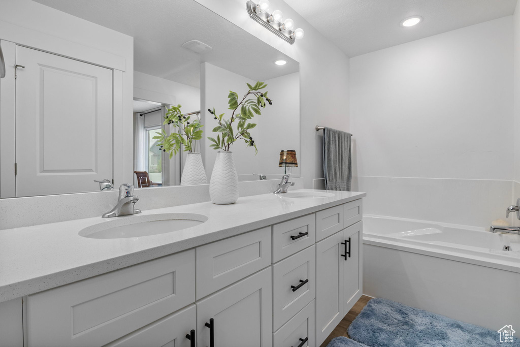 Bathroom with double vanity, a garden tub, recessed lighting, and wood finished floors