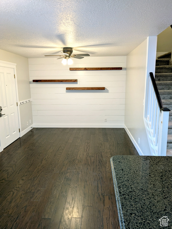 Unfurnished living room with baseboards, dark wood-style flooring, a textured ceiling, stairs, and wooden walls