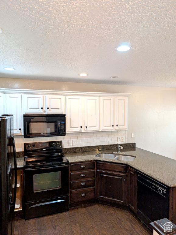 Kitchen featuring black appliances, a sink, white cabinets, dark wood-type flooring, and dark countertops