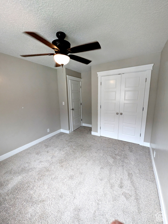 Unfurnished bedroom featuring carpet, a textured ceiling, baseboards, a closet, and ceiling fan