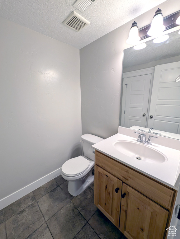 Half bathroom with toilet, vanity, a textured ceiling, and baseboards