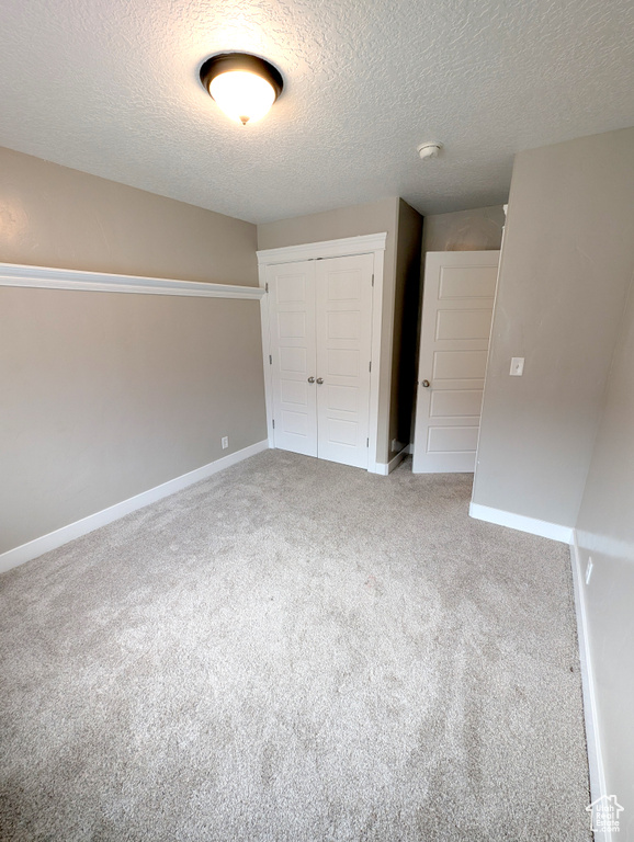 Unfurnished bedroom featuring a closet, carpet flooring, a textured ceiling, and baseboards