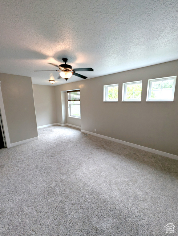 Empty room featuring a textured ceiling, baseboards, a ceiling fan, and light carpet