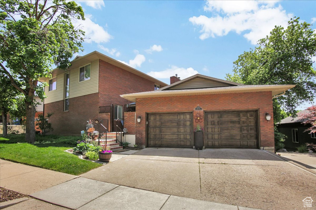 View of front of property featuring brick siding, an attached garage, concrete driveway, a front lawn, and a chimney