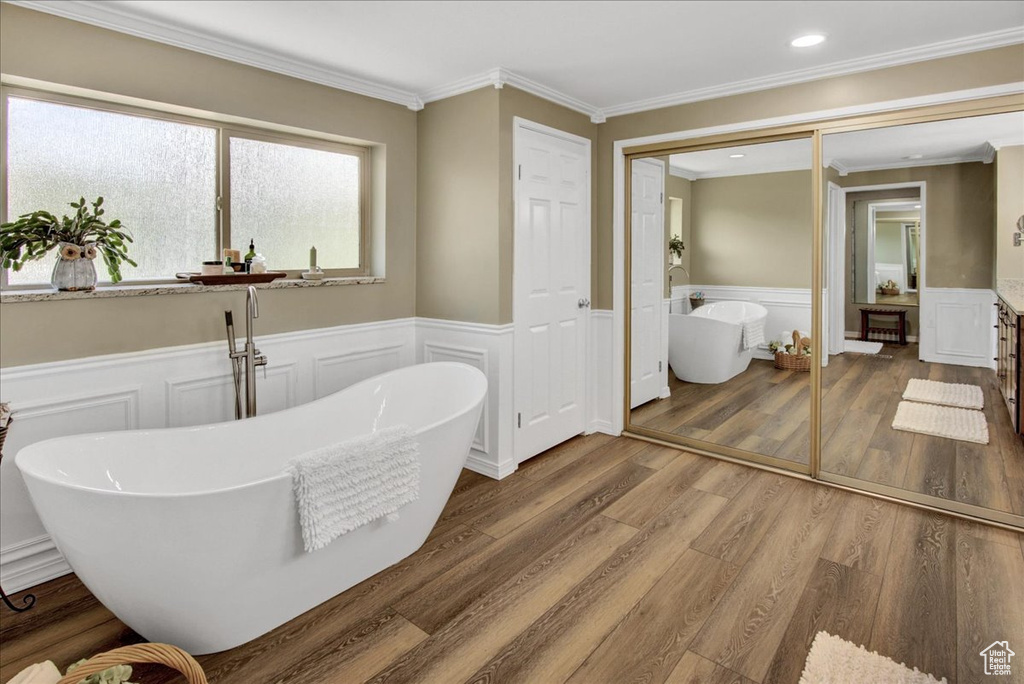 Full bathroom featuring a wainscoted wall, a decorative wall, ornamental molding, a soaking tub, and wood finished floors