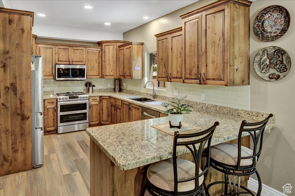 Kitchen with stainless steel appliances, a sink, a peninsula, brown cabinetry, and light wood finished floors