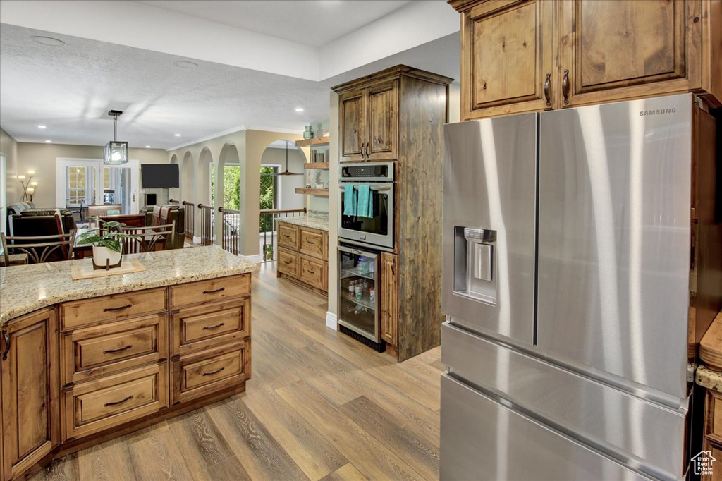 Kitchen featuring stainless steel appliances, wine cooler, arched walkways, light wood finished floors, and brown cabinets