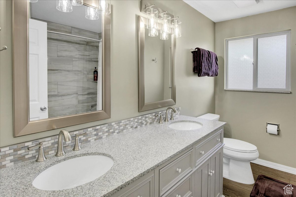 Bathroom featuring toilet, wood finished floors, baseboards, and double vanity