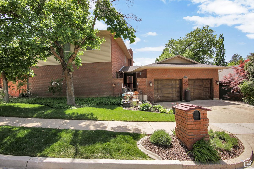 View of front of home featuring brick siding, an attached garage, a front lawn, and driveway