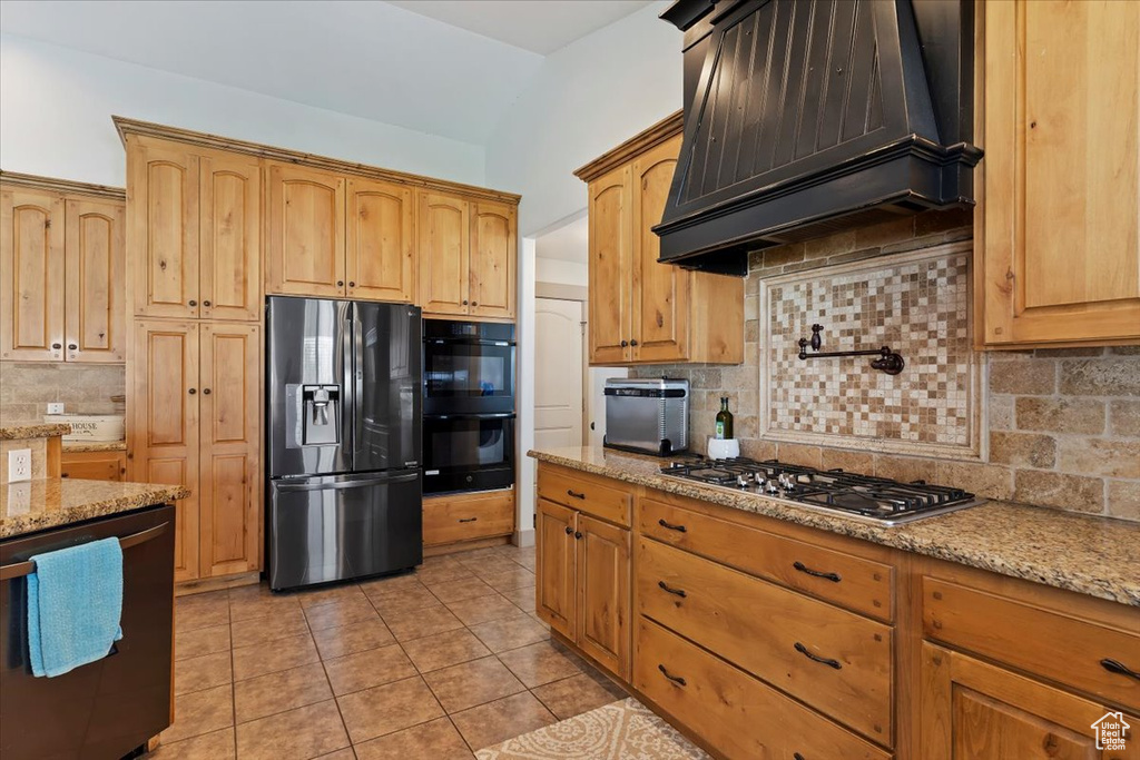 Kitchen featuring black appliances, premium range hood, tasteful backsplash, light stone countertops, and light tile patterned floors