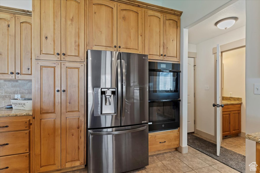 Kitchen with stainless steel fridge, light tile patterned flooring, light stone counters, and tasteful backsplash