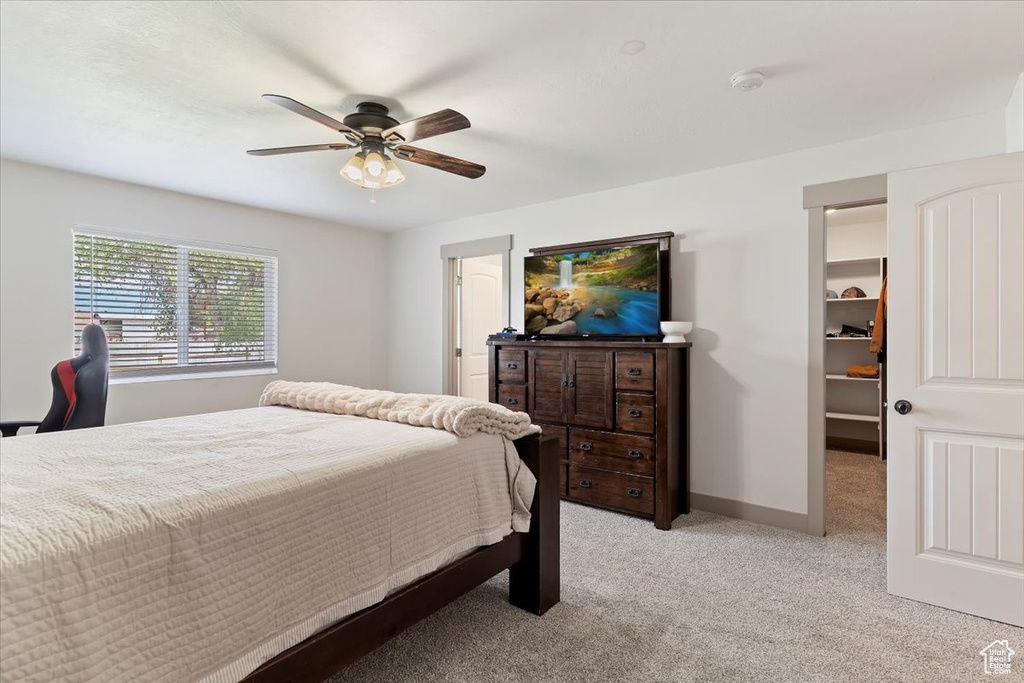Bedroom with light carpet, a walk in closet, ceiling fan, and baseboards