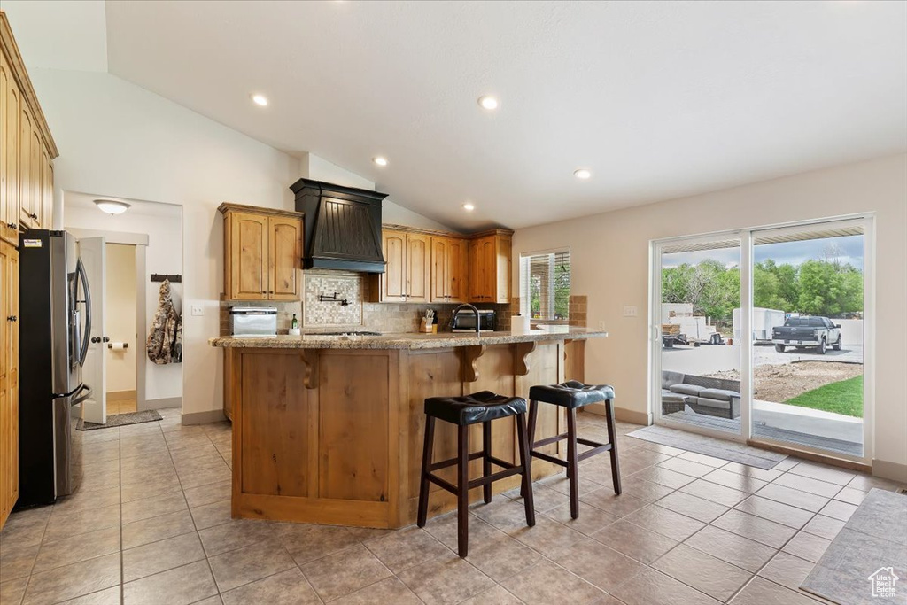 Kitchen featuring appliances with stainless steel finishes, vaulted ceiling, premium range hood, tasteful backsplash, and light tile patterned flooring