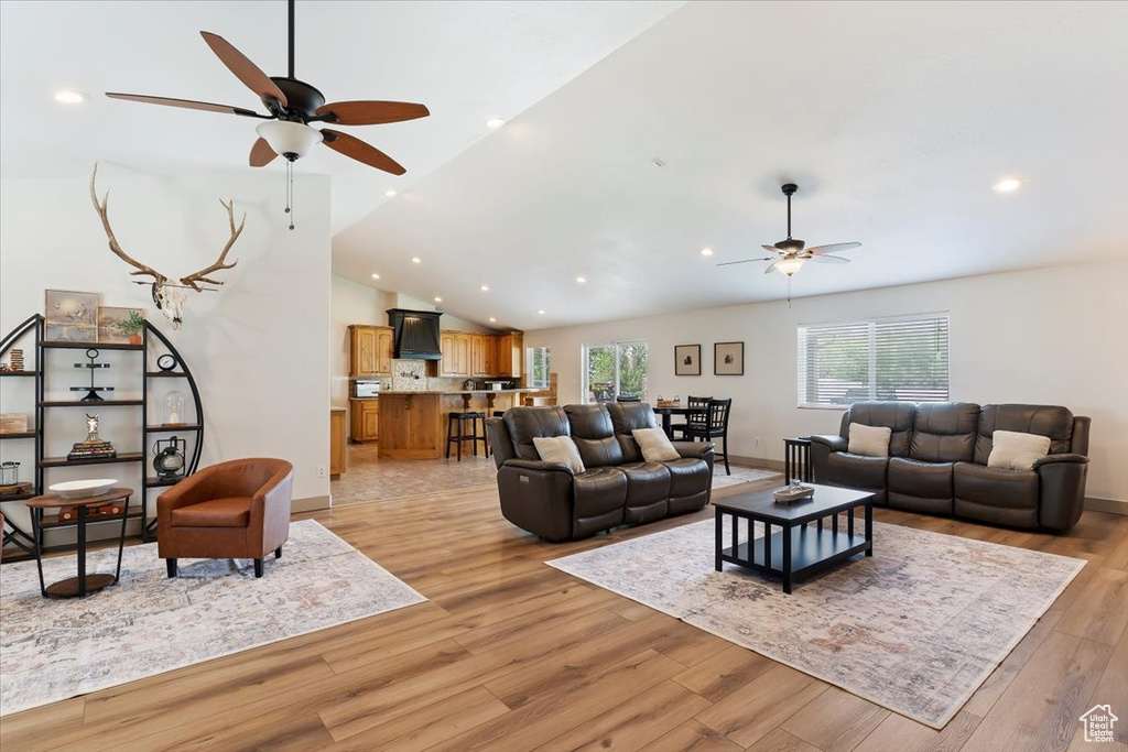 Living room with a ceiling fan, lofted ceiling, light wood-style flooring, baseboards, and recessed lighting