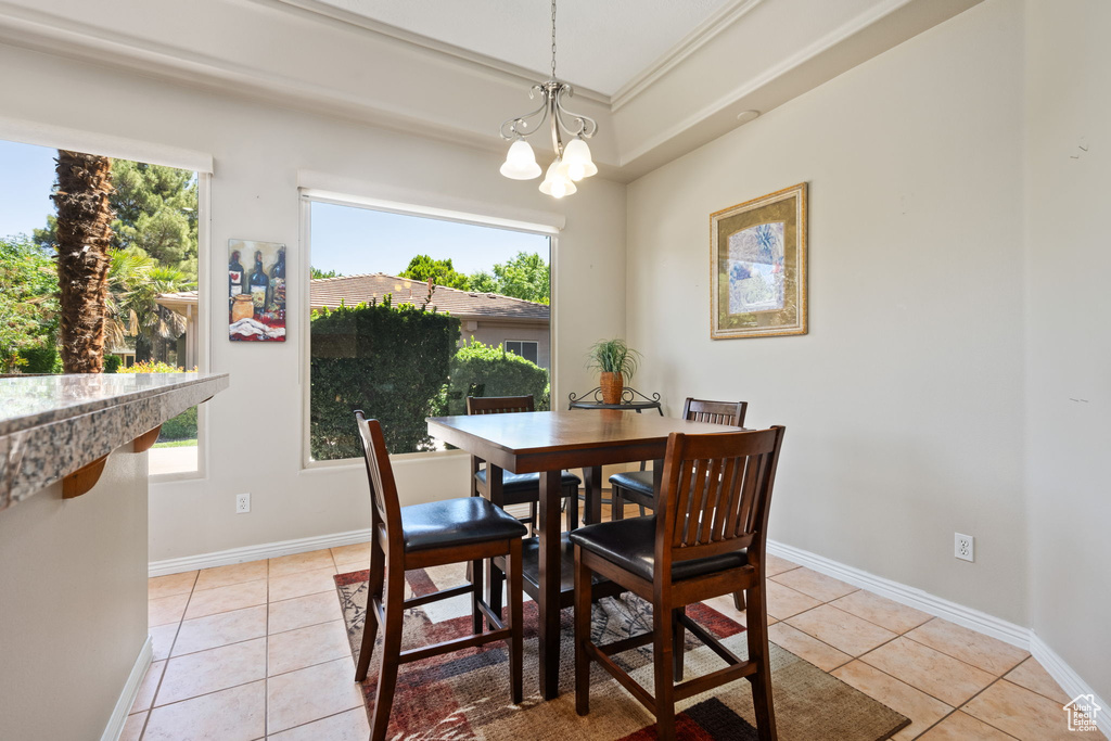 Dining area with light tile patterned floors, healthy amount of natural light, baseboards, ornamental molding, and a chandelier