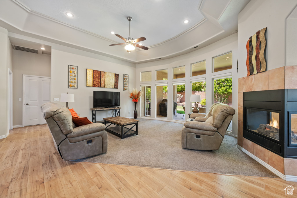 Living area with a fireplace, light wood-type flooring, recessed lighting, ceiling fan, and a tray ceiling