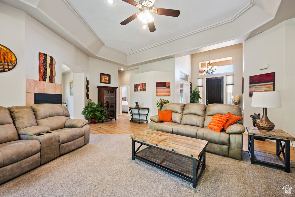 Carpeted living area featuring a towering ceiling, a ceiling fan, arched walkways, a tile fireplace, and a chandelier