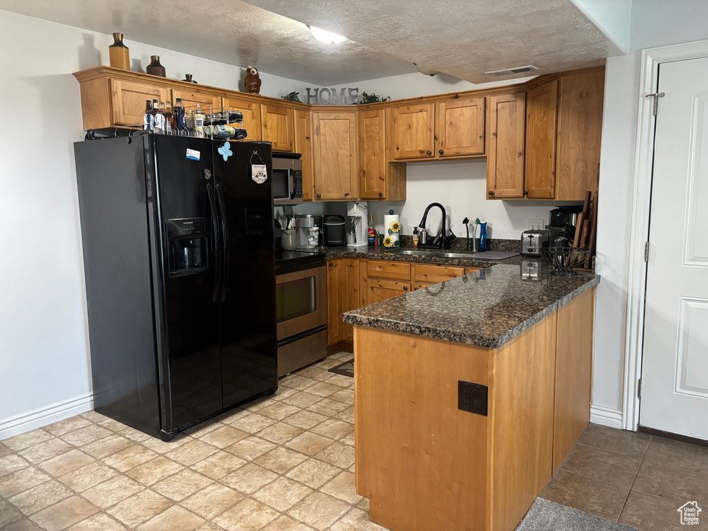 Kitchen featuring appliances with stainless steel finishes, a sink, a peninsula, brown cabinets, and a textured ceiling
