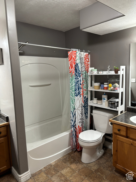 Full bath with vanity, a textured ceiling, toilet, stone finish flooring, and shower / bath combo with shower curtain