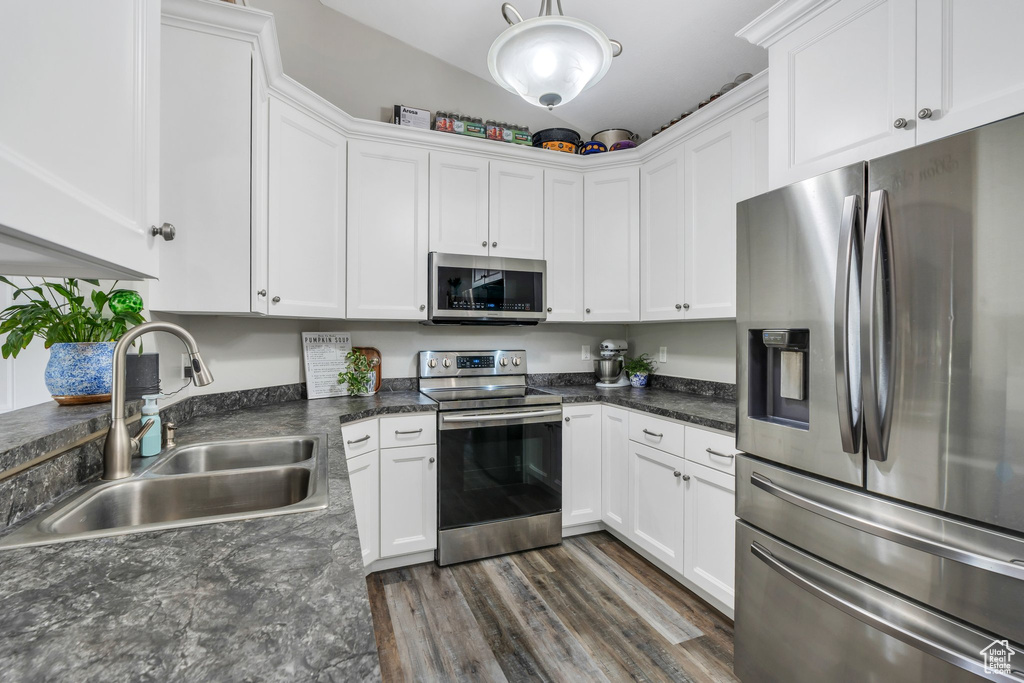 Kitchen with stainless steel appliances, a sink, white cabinetry, and lofted ceiling